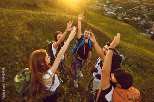 High angle of team of happy tourists reaching out for high five while hiking on grassy hill