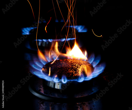 Closeup shot of blue fire from domestic kitchen stove top. Gas cooker with burning flames of propane gas. Red sparks.