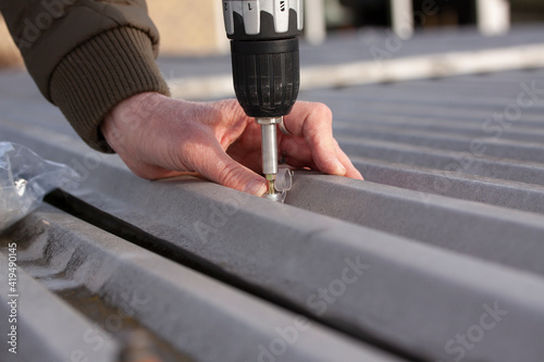 Fényképezés Woman mounting old rapezoidal metal roof using a power drill and screws  with clear caps