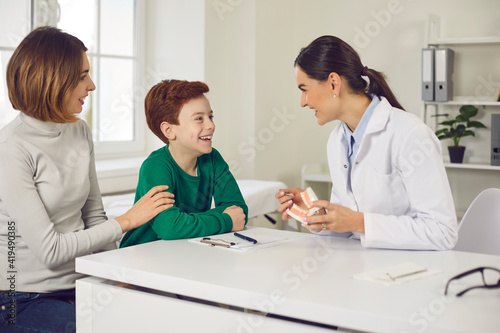 Friendly pediatric dentist consults mother with her young son in the office of a modern dental clinic. Mother and child discuss dental treatment plan. Concept of painless treatment of children's teeth