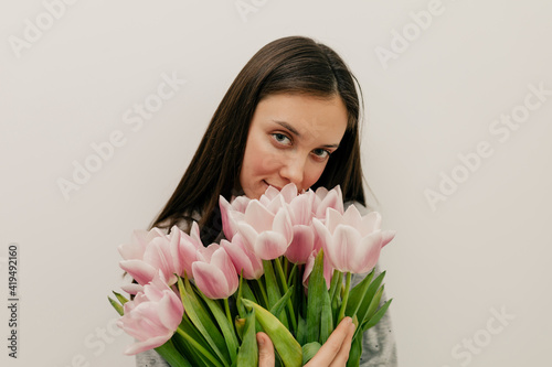 Indoor portrait of beautiful young lady with bouquet of pink flowers over isolated background