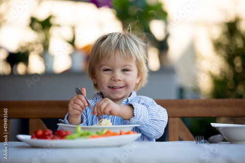 Cute child, toddler blond boy, eating spaghetti in garden