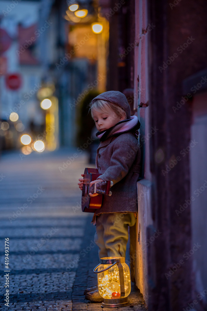 Obraz premium Sweet toddler boy, playing guitar at night in the city with teddy bear toy