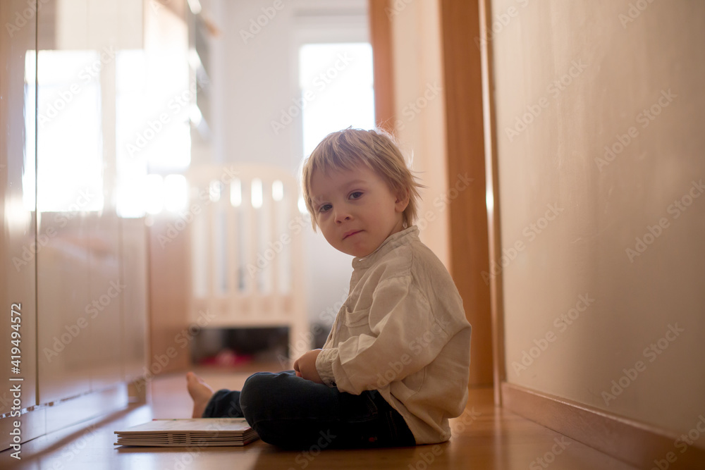 Beautiful toddler blond boy, lying on the floor at home in the hall, reading book Beautiful toddler blond boy, lying on the floor at home in the hall, reading book