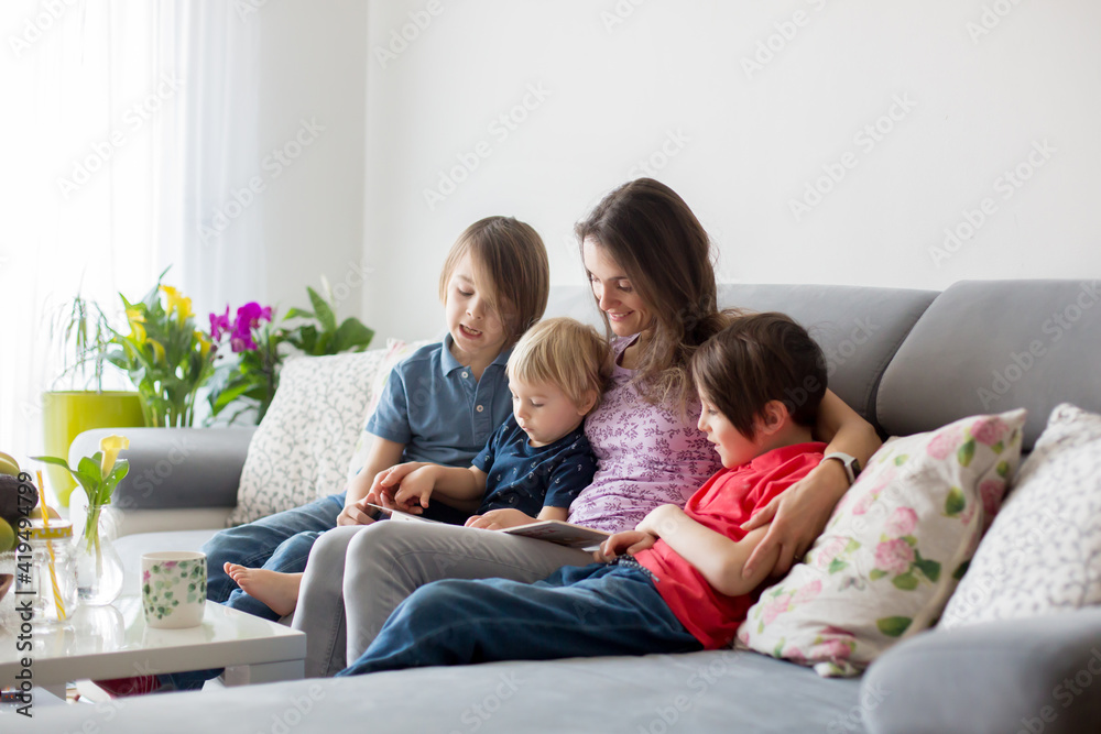 Young woman, mother with three kids, reading a book at home, hugging and laughing