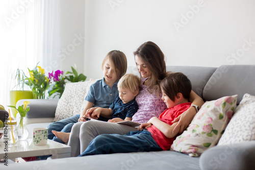 Young woman, mother with three kids, reading a book at home, hugging and laughing