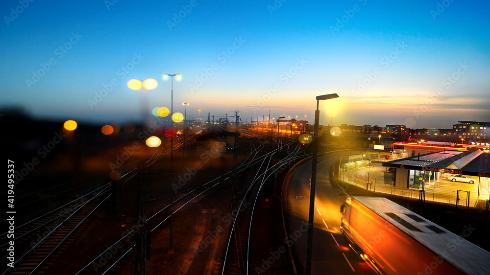 Traffic and transport at night in the city - rails and streets - gas and train station with truck and lights in motion
