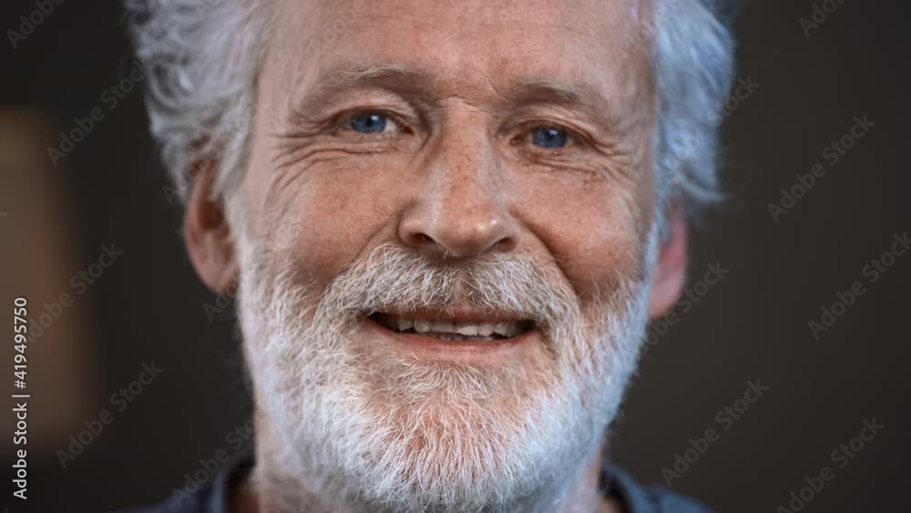 Portrait of a senior old man with gray hair looking at the camera. Happy elderly man smiling. Gray beard and home clothes. Grandpa is happy to live, a healthy lifestyle. Close-up