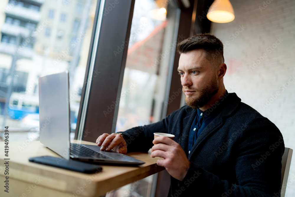 Fototapeta premium Stylish businessman doing work in beautiful cafe. Cup of cofee and phone is near him.
