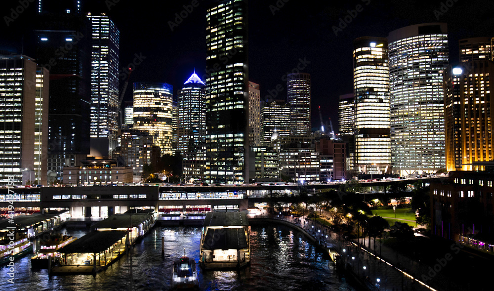 Fototapeta premium Night view of Downtown Sydney Skyline. Illuminated Highrises and Office Towers. Sydney Ferry wharf area.