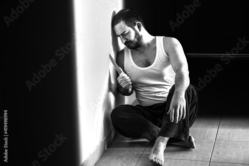 Man sitting on the ground with a knife and leaning against the wall