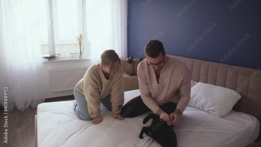 Happy couple relaxes after moving in a new home. Couple have fun on bed with a black cat Happy couple relaxes after moving in a new home. Couple have fun on bed with a black cat