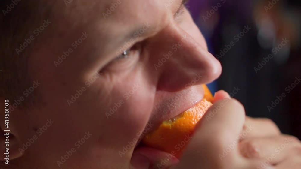 Hungry young man greedily eats orange Hungry young man greedily eats orange