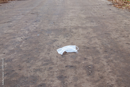 Dirty used disposable medical face mask dumped as garbage on asphalt street. Waste during COVID-19. Pollution due coronavirus pandemic