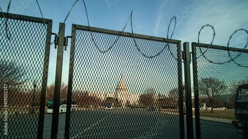A time-lapse of the U.S. Capitol building at sunset, fortified behind a metal fence topped with razor wire to address security concerns following the January 6th 2021 insurrection. Camera dolly out. 