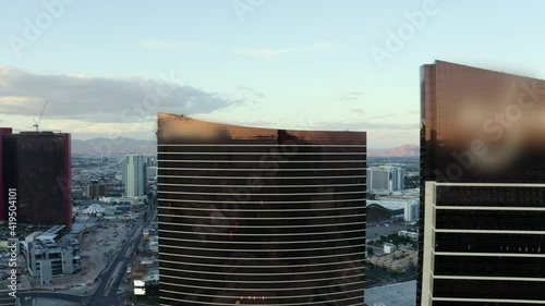 Aerial: Towering Black Glass Hotels Stand High Above Downtown Las Vegas With Distant Casinos At Dusk