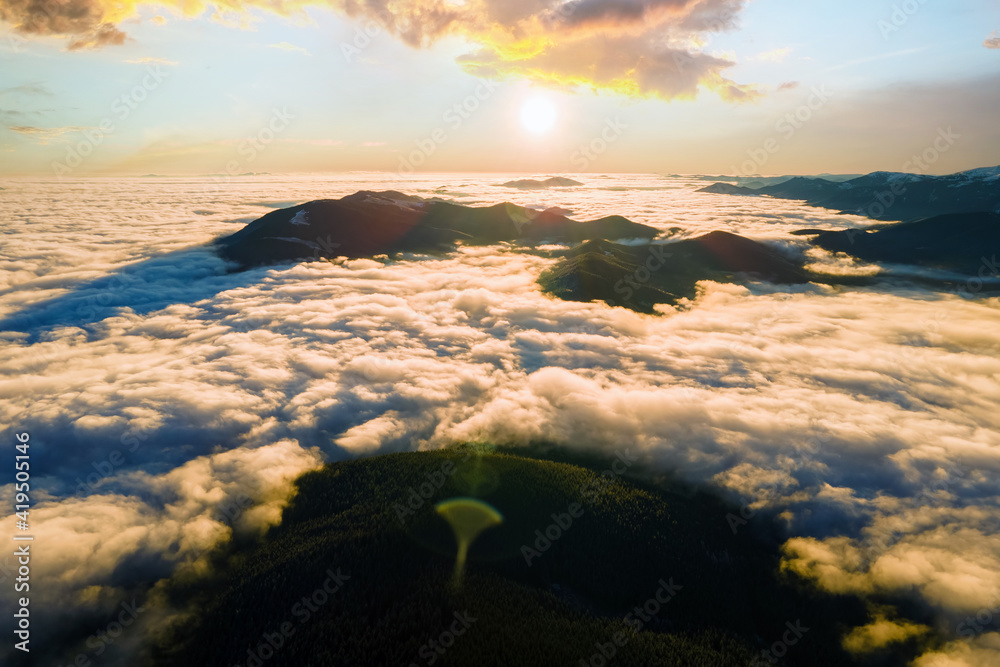 Aerial view of vibrant sunrise over mountain hills covered with evergreen spruce forest in autumn.