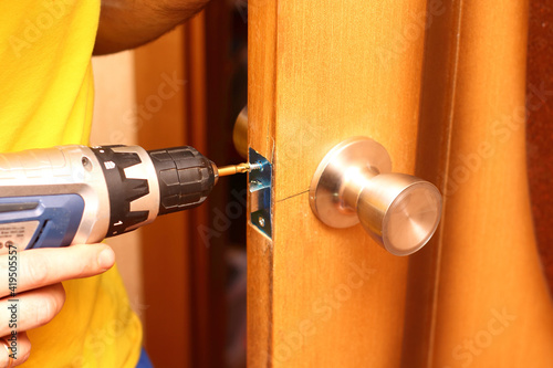 Worker installing or repairing new lock and door knob with screwdriver