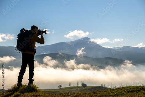 Silhouette of a backpacker photographer taking pictures of morning landscape in autumn mountains with digital camera. © bilanol