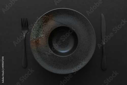 Top view  of empty black ceramic plate for pasta, with an abstract pattern and black cutlery on a black background. Flat lay. Minimal design concept.