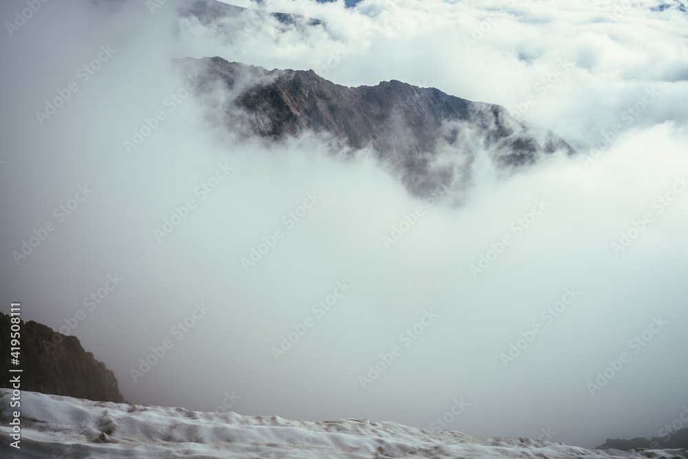 Wonderful mountain scenery with great rocks in dense low clouds. Atmospheric mountain landscape with big rocky mountains above clouds. Beautiful view from snowy top to high rocks over thick clouds.