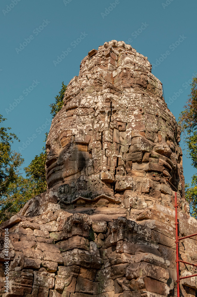 Fototapeta premium VIEWS OF ANKOR WAT TEMPLES - TOWERS WITH FACES- VEGETATION GROWING OVER BUILDINGS. COLORED RUINS, TEMPLES WITH HISTORY AND INCREDIBLE ARCHITECTURE