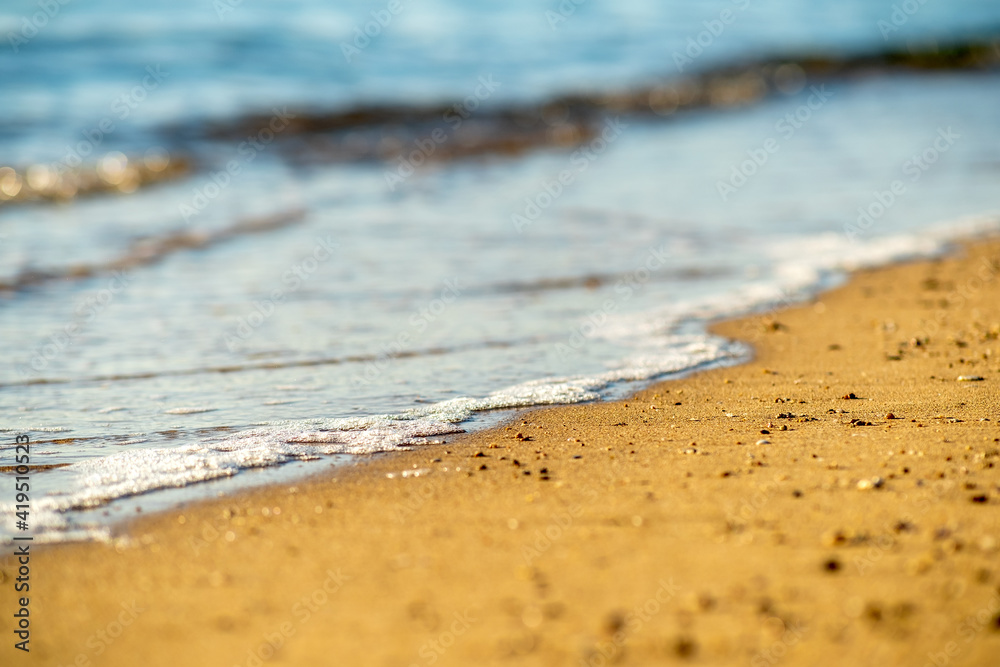 Close up of small sea waves with clear blue water over yellow sand beach at summer sunny shore. Close up of small sea waves with clear blue water over yellow sand beach at summer sunny shore.