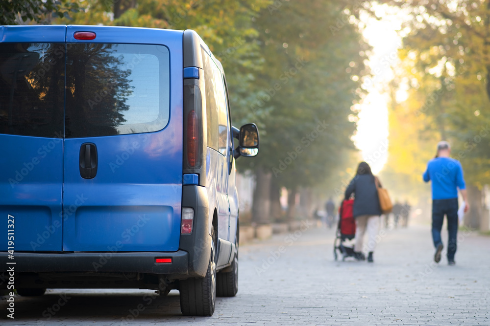 Passenger van car parked on a city alley street side with blurred walking pedestrians in autumn.