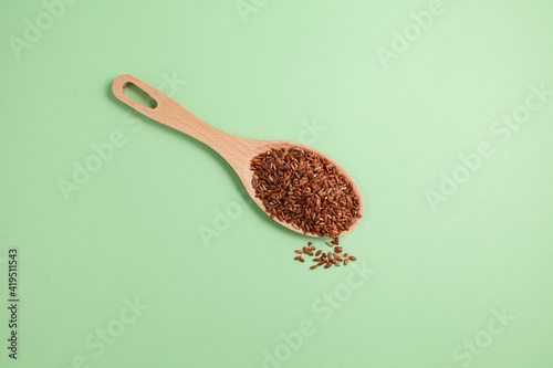 Brown GABA rice in wooden spoon on green background, top view. Selective focus, copy space