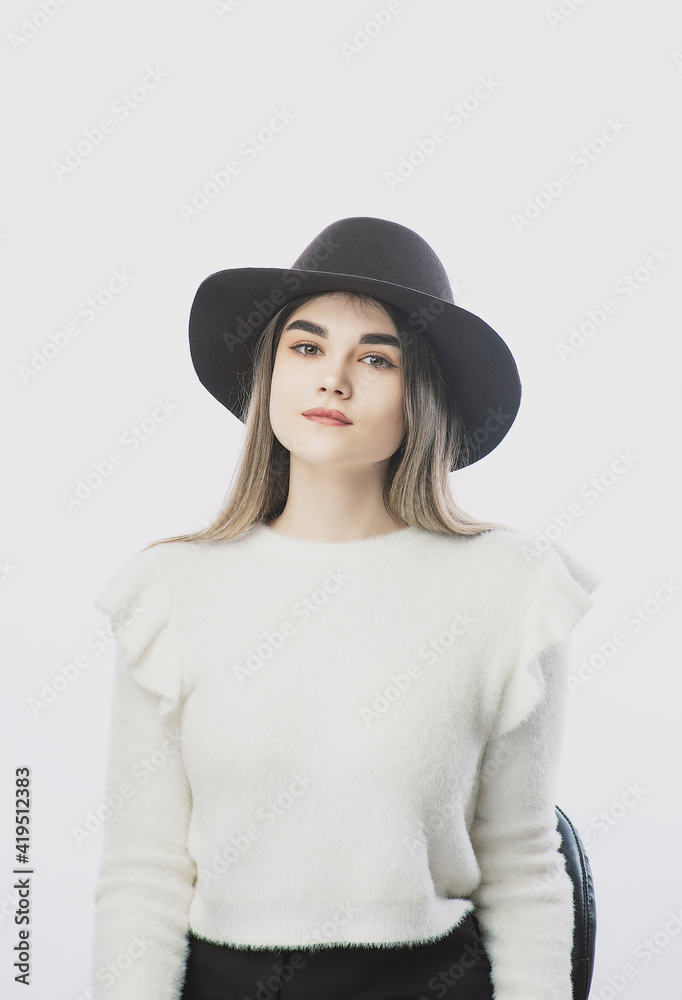 girl in a white sweater posing in a felt hat on a light background