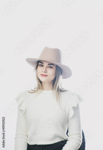 girl in a white sweater posing in a felt hat on a light background