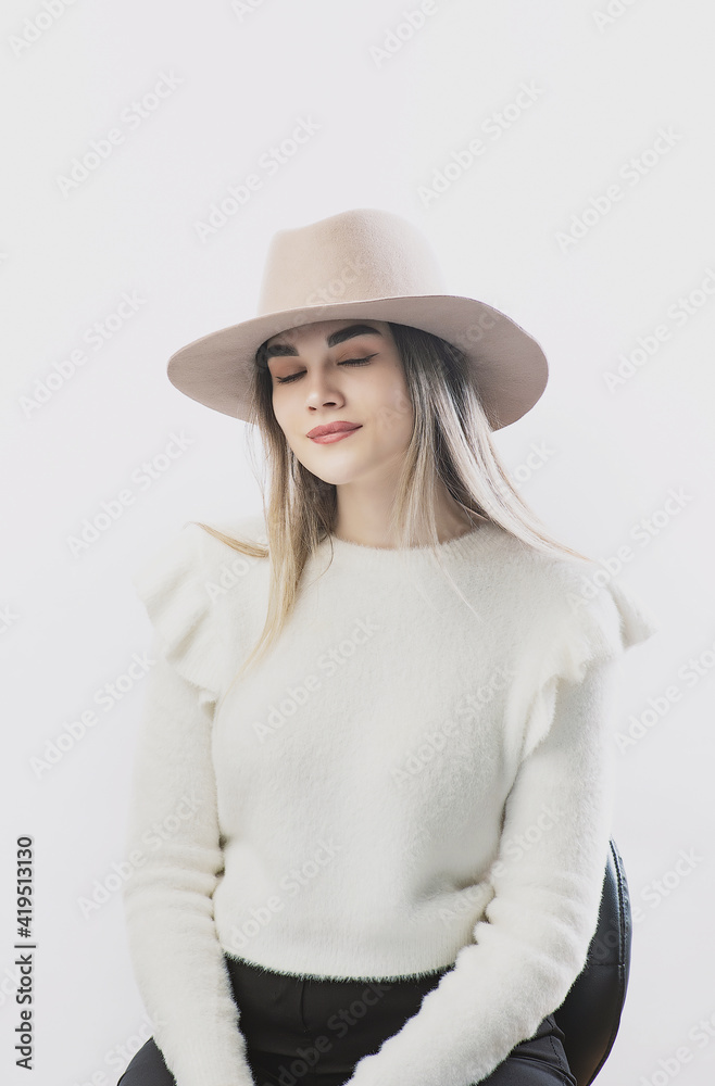 girl in a white sweater posing in a felt hat on a light background girl in a white sweater posing in a felt hat on a light background