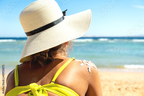Back view of young woman tanning at the beach with sunscreen cream in sun shape on her shoulder. UV sunburn protection and sunblock skincare concept