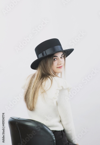 girl in a white sweater posing in a felt hat on a light background