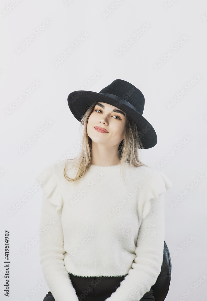 girl in a white sweater posing in a felt hat on a light background girl in a white sweater posing in a felt hat on a light background