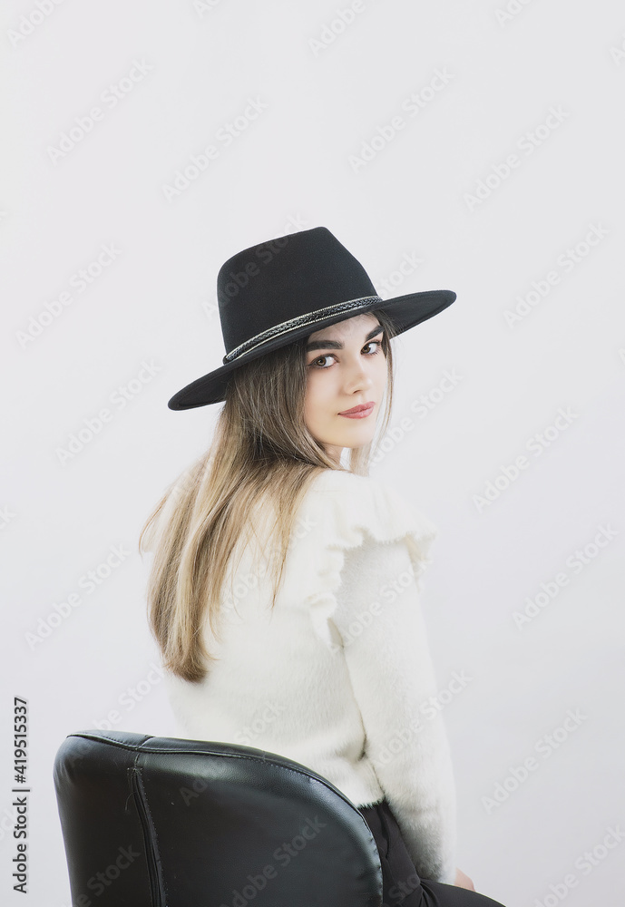 girl in a white sweater posing in a felt hat on a light background girl in a white sweater posing in a felt hat on a light background