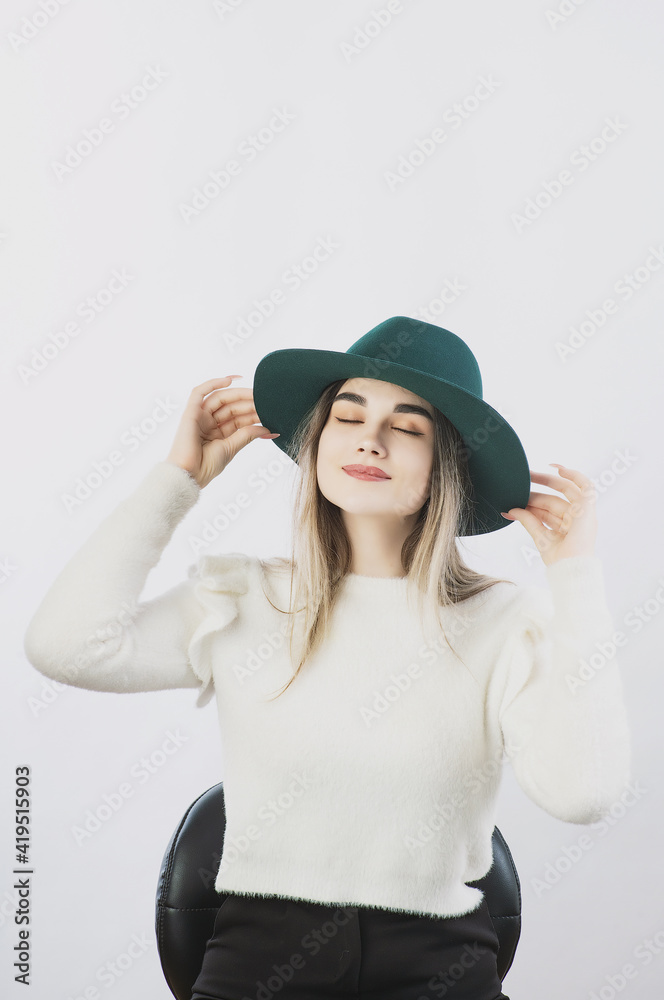 girl in a white sweater posing in a felt hat on a light background