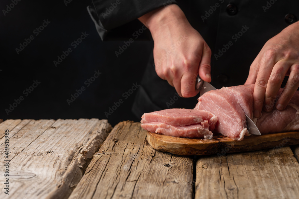 Chef cuts fresh pork fillet. On a dark background. Banner, sale and preparation of meat, recipes and menus.