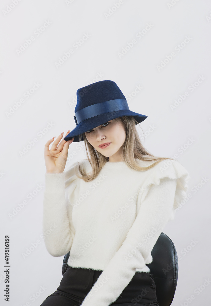 girl in a white sweater posing in a felt hat on a light background
