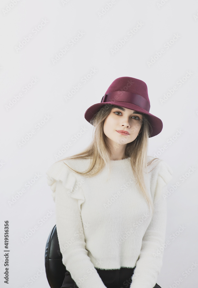 girl in a white sweater posing in a felt hat on a light background girl in a white sweater posing in a felt hat on a light background