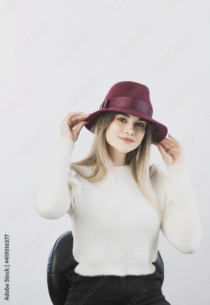 girl in a white sweater posing in a felt hat on a light background girl in a white sweater posing in a felt hat on a light background