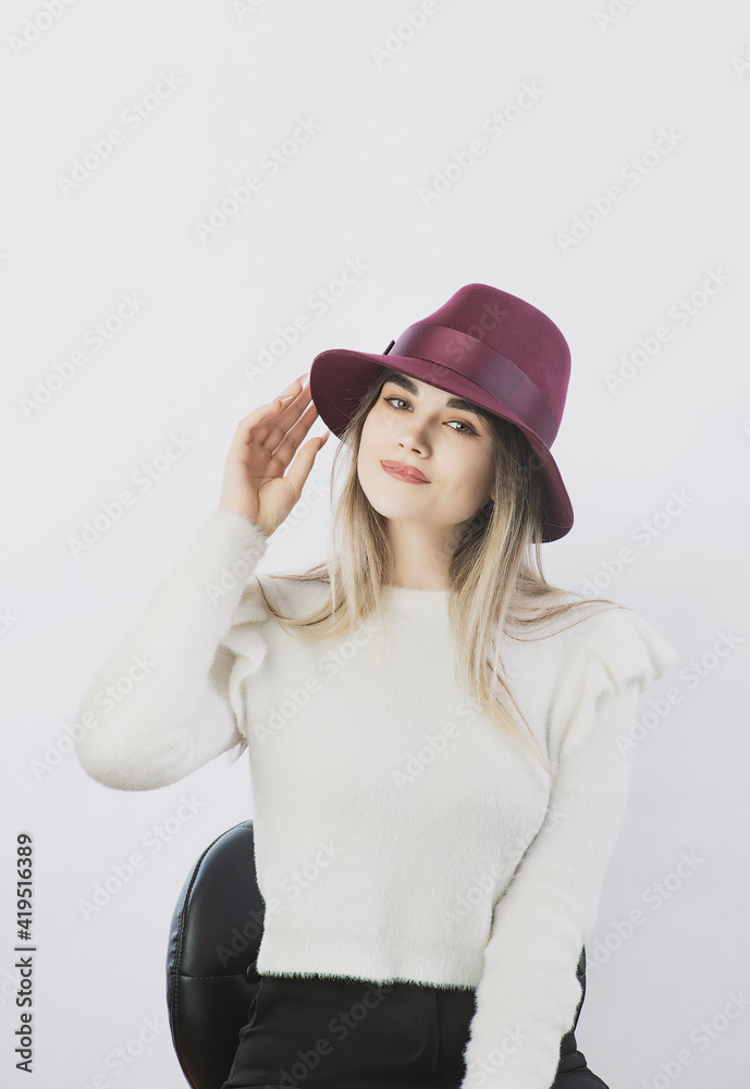 girl in a white sweater posing in a felt hat on a light background girl in a white sweater posing in a felt hat on a light background