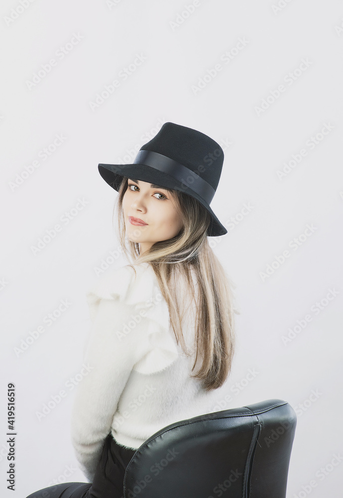 girl in a white sweater posing in a felt hat on a light background girl in a white sweater posing in a felt hat on a light background