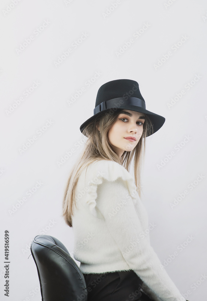 girl in a white sweater posing in a felt hat on a light background girl in a white sweater posing in a felt hat on a light background