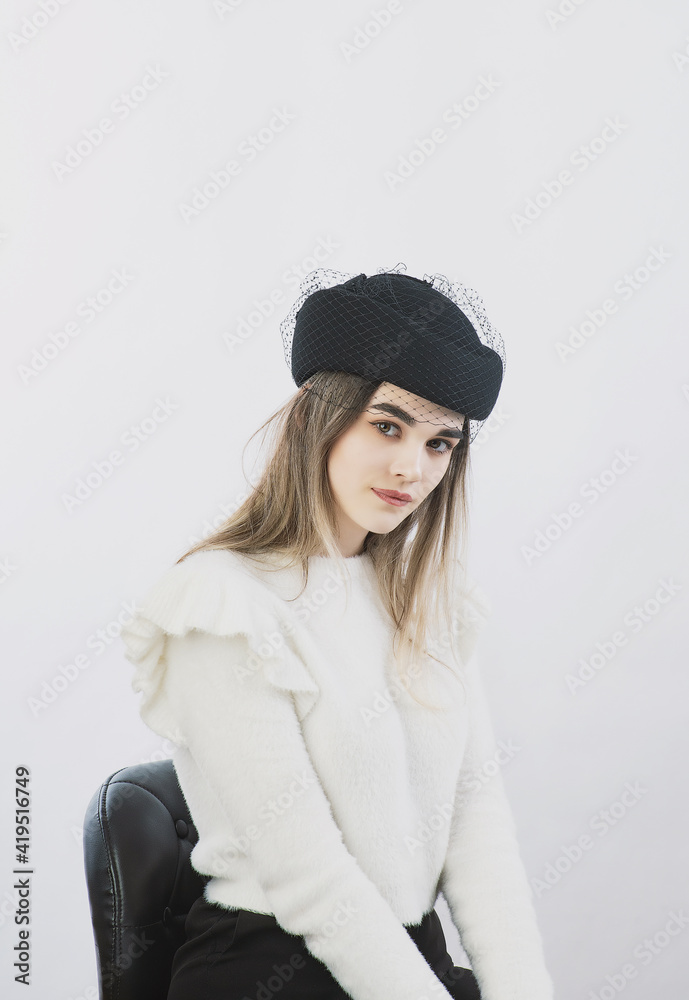 girl in a white sweater posing in a felt hat on a light background