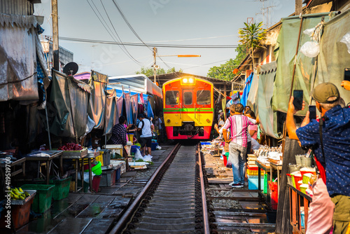 Train on Tracks Moving Slow. Umbrella Fresh Market on the Railroad Track, Mae Klong Train Station, Bangkok, Thailand on a Sunny Day. © kaycco
