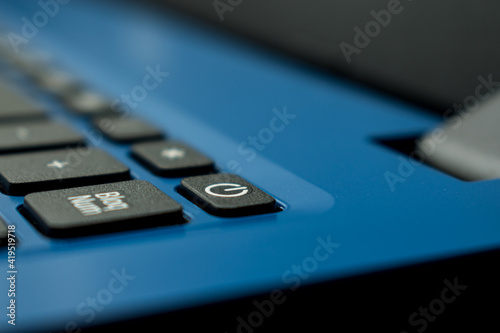 Closeup of a black power button on a blue laptop in a office 