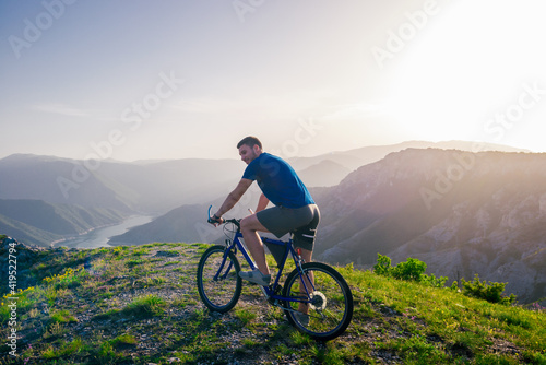 Adventurous Cyclist riding his mountain bike at the edge of a cliff, on rocky terrain while wearing no safety equipment.Amazing top view.