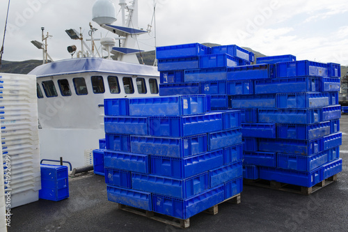 Plastic fish boxes lying on the ground by the Scottish seaside, with fishermen's boats in the background — everyday tools used for sorting and transporting the catch