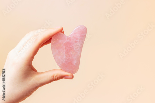 A female hand holding gua sha face massager on brown background.